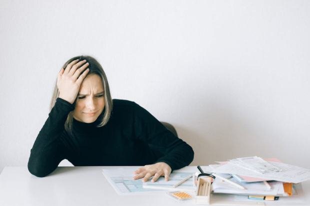 Woman in black sweater stressed with financial paperwork, overwhelmed at white table.