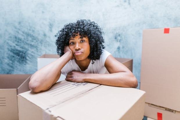Tired woman leaning on a moving box while packing and relocating to a new home.